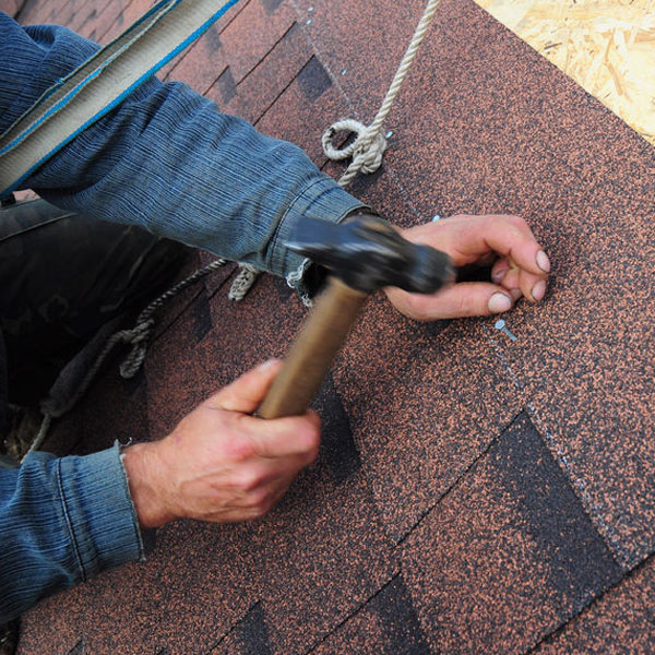 close up of man hammering a nail into shingles